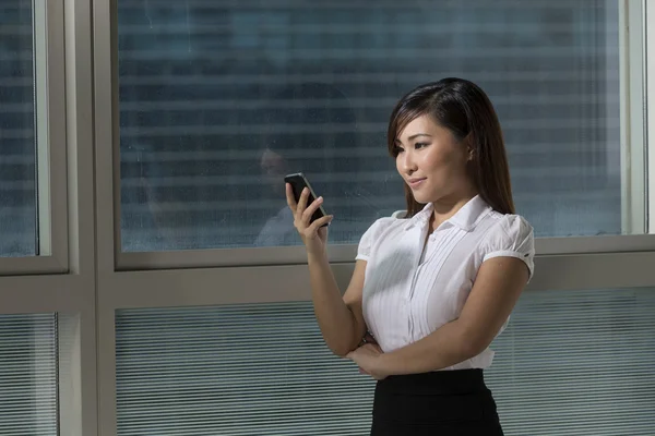 Asian businesswoman using phone and looking out of office window