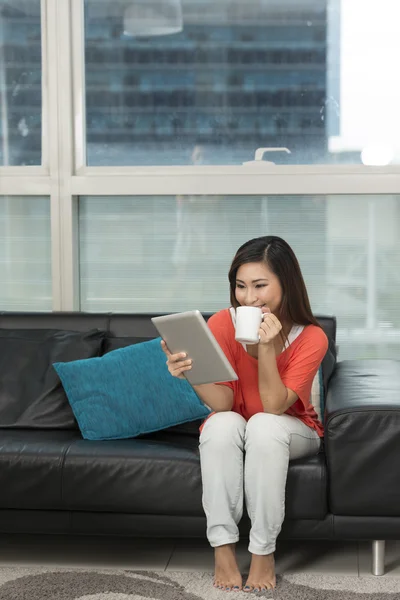 Asian woman at home reading a tablet PC.