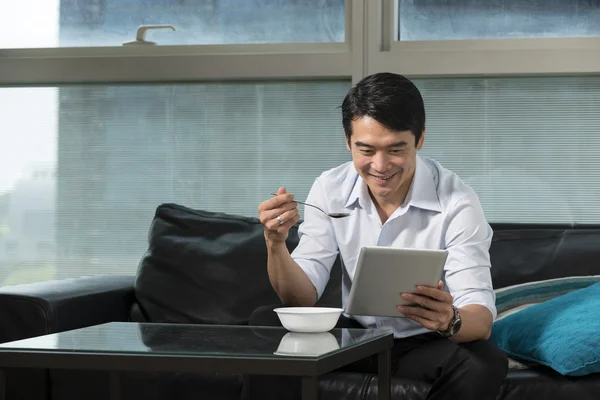 Asian Businessman eating breakfast and reading his tablet.