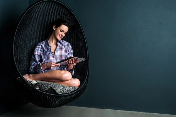 Pretty woman on bubble chair reading magazine