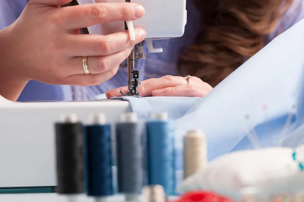 Hands on sewing machine with reels of colour threads and sewing