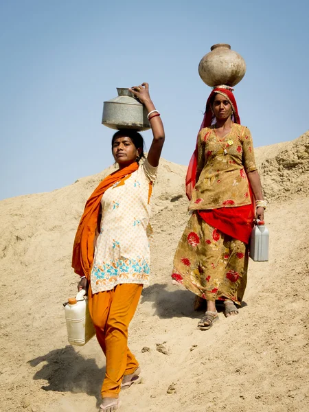 Two Indian women carrying water in the desert.