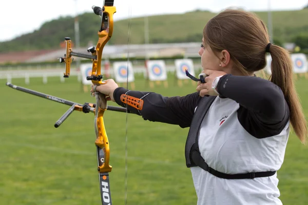 An unidentified female competitor is shooting with a bow and an arrow.