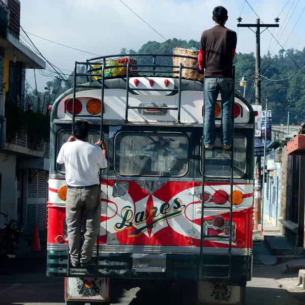 Two men are standing on two ladders outside of an old colored bus.