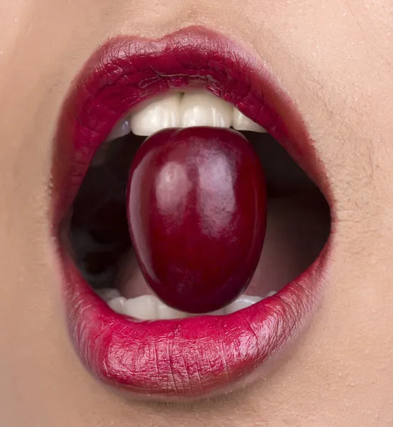 Closeup of woman mouth eating red grape.