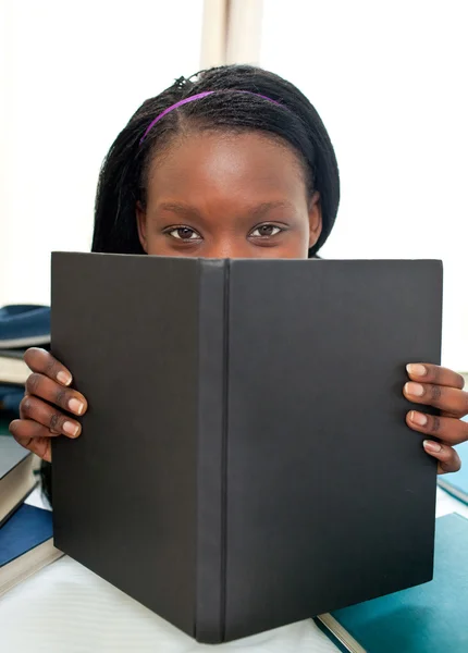 Cute afro-american teenager behind a book looking at the camera