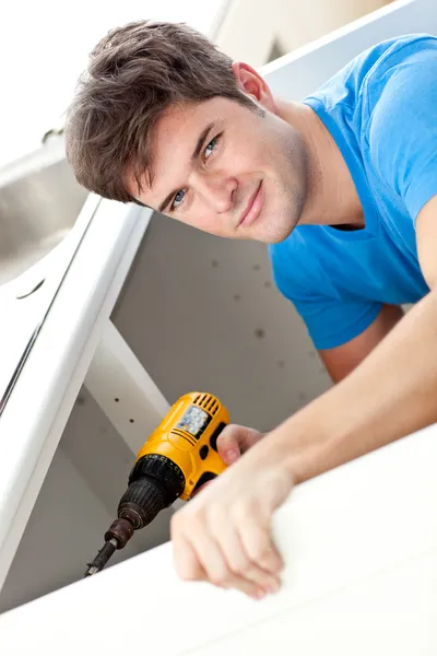 Charismatic man repairing his sink and holding a drill in the ki