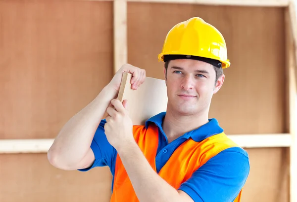 Assertive young male worker with a yellow helmet carrying a wood