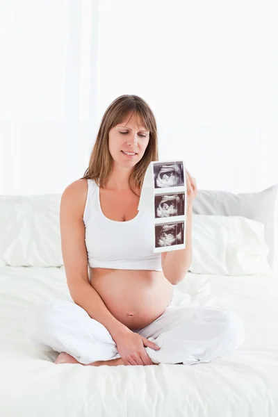 Pretty pregnant female showing an ultrasound scan while sitting