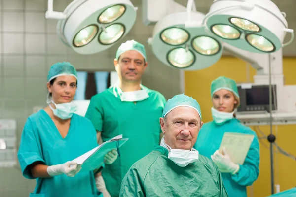 Smiling surgeon sitting with a team behind him