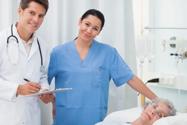 Doctor and nurse looking at camera next to a patient lying