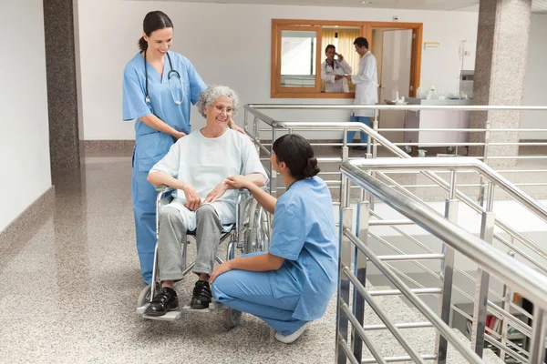 Two nurses talking with old women sitting in wheelchair