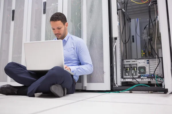 Man sitting on floor with laptop beside servers