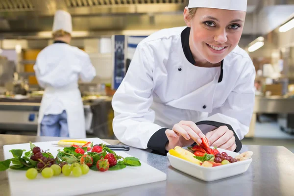 Smiling chef putting a strawberry in the fruit bowl