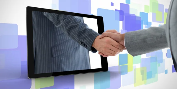 Businessman reaching out from tablet and shaking hands with other man
