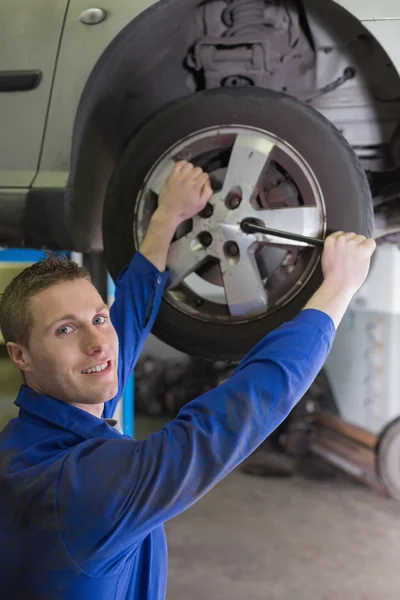 Male mechanic fixing car tire with wrench