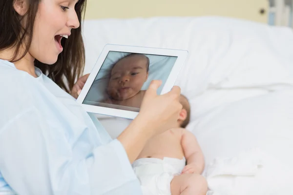 Smiling mother using a tablet to take a picture of a newborn bab