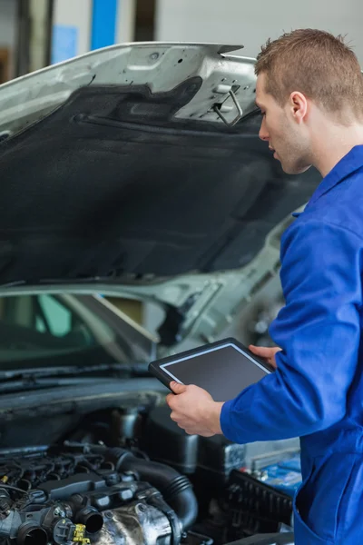 Mechanic with tablet pc examining car engine