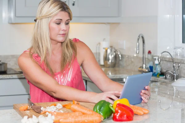 Woman cooking whilst looking at digital tablet in kitchen