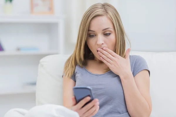 Casual shocked woman looking at cellphone at home