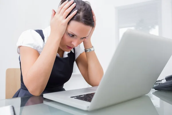 Upset business woman with head in hands in front of laptop at of