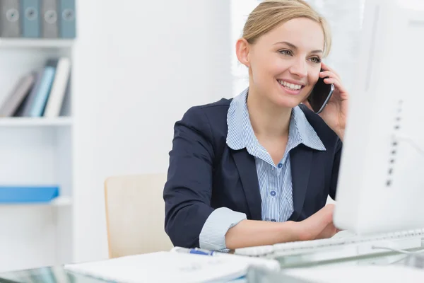 Happy business woman using computer while on call at desk