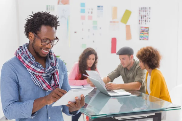 Smiling man using tablet with creative team working behind