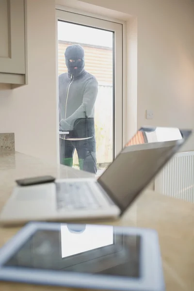 Burglar opening kitchen door and looking at laptop