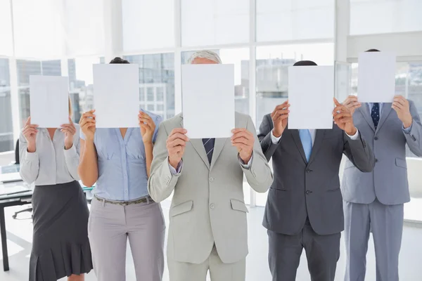 Buisness team holding up blank pages and covering their faces