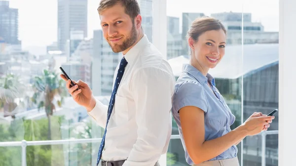 Smiling business team standing back to back and texting