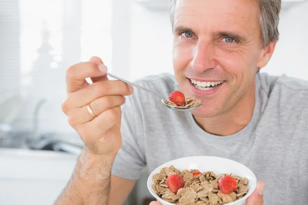 Cheerful man eating cereal for breakfast