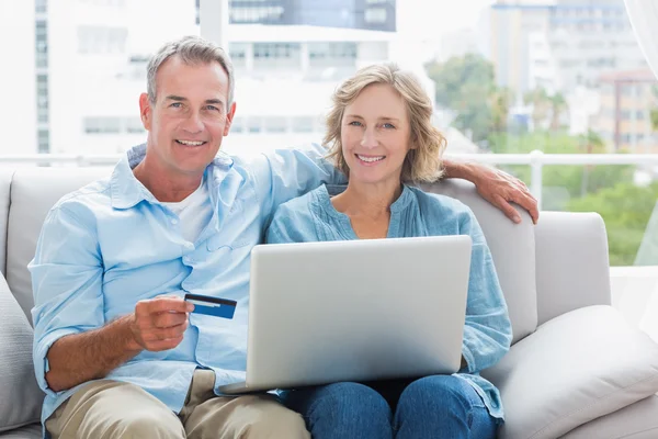 Happy couple sitting on their couch using the laptop to buy onli
