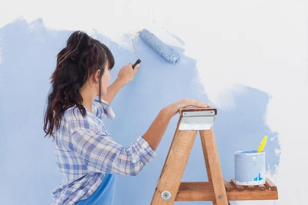 Woman using paint roller to paint wall