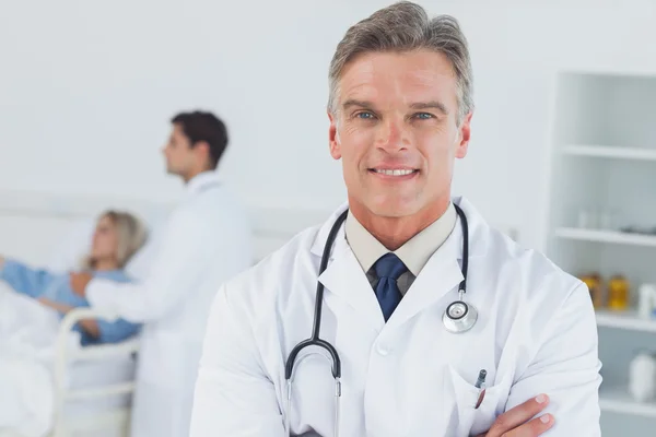 Experienced doctor posing with doctor attending patient on backg