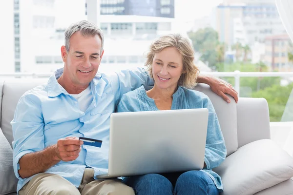 Smiling couple sitting on their couch using the laptop to buy on