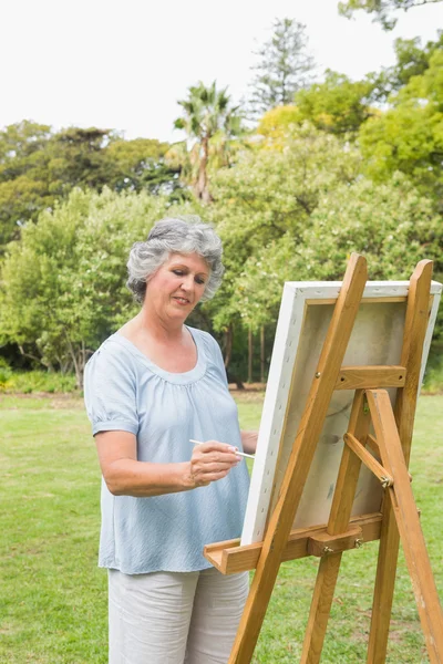 Happy retired woman painting on canvas