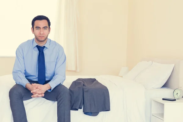 Stern man looking at camera sitting on his bed