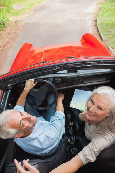 Mature couple in red convertible looking at camera