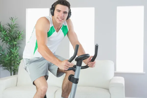 Smiling handsome man training on exercise bike listening to music