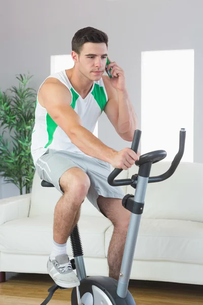 Stern handsome man training on exercise bike phoning