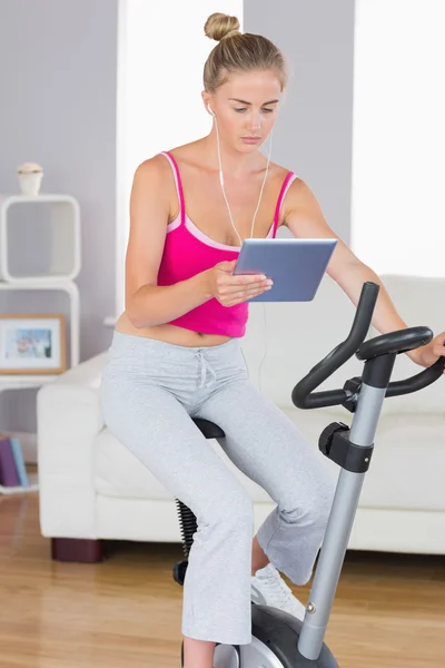 Sporty serious blonde training on exercise bike using tablet