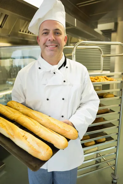 Mature baker presenting proudly some baguettes on a baking tray