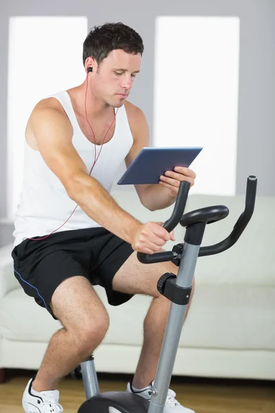 Handsome sporty man exercising on bike and using tablet