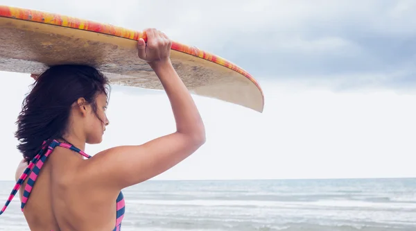 Woman carrying surfboard on head at beach