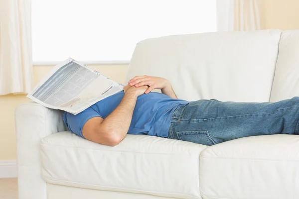 Casual man sleeping on couch with newspaper on his head