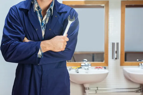 Plumber in blue boiler suit posing with wrench