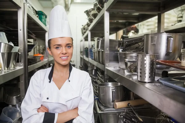 Young cheerful chef standing arms crossed between shelves