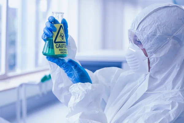 Ccientist in protective suit with hazardous chemical in flask at