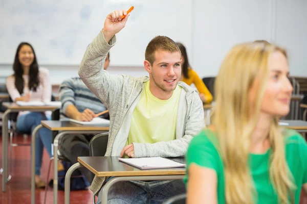 Male student raising hand by others in classroom
