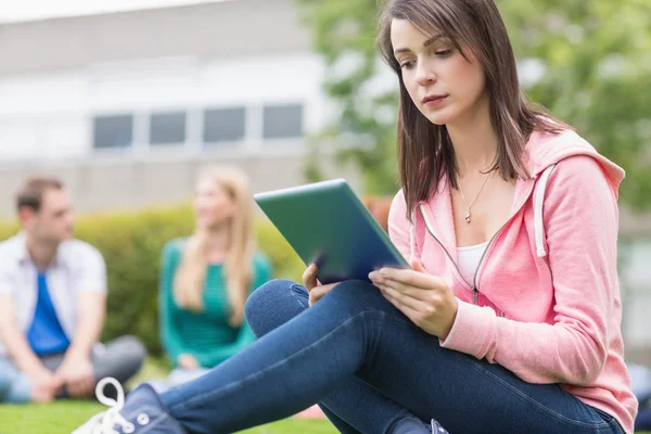 College girl using tablet PC with blurred students in park